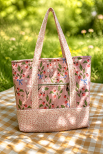 A pink fabric tote bag with a strawberry and floral print, featuring two shoulder straps and a front zippered pocket and two interior pockets, base and straps are tiny heart design. choose from recessed zipper or magnetic snap.