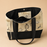 A tote bag with a vintage Paris-themed print featuring the Eiffel Tower, postcards, and script, with solid black straps and a solid black bottom.
