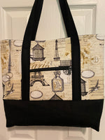 A tote bag with a vintage Paris-themed print featuring the Eiffel Tower, postcards, and script, with solid black straps and a solid black bottom.